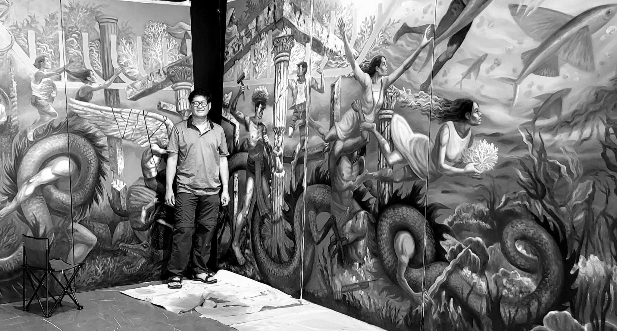 Jeho Bitancor standing before a monumental mural in progress, dwarfed by his own imagery of columns, angels, and sea serpents